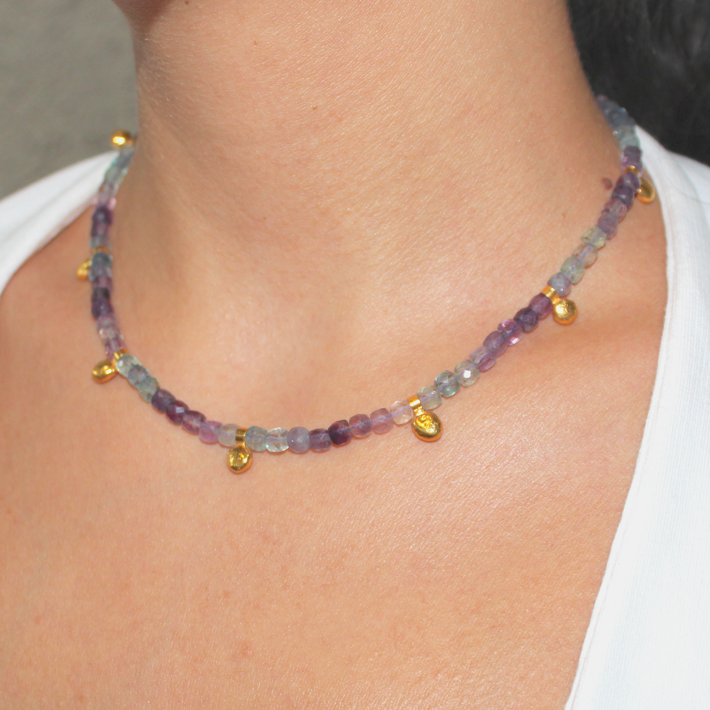 Necklace with multicolored fluorite beads and gold charms worn by a person