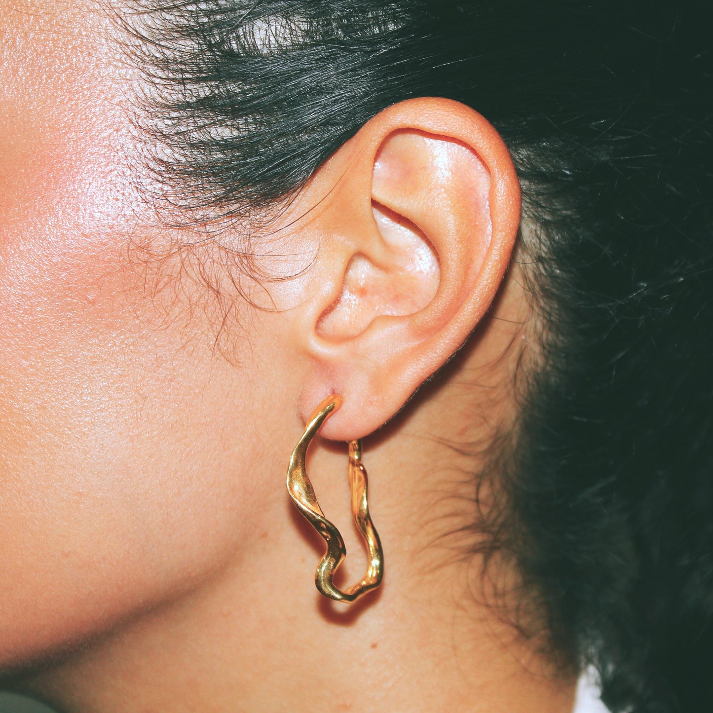 Close-up of a person wearing a gold hoop earring with a neutral background handmade jewelry lisbon