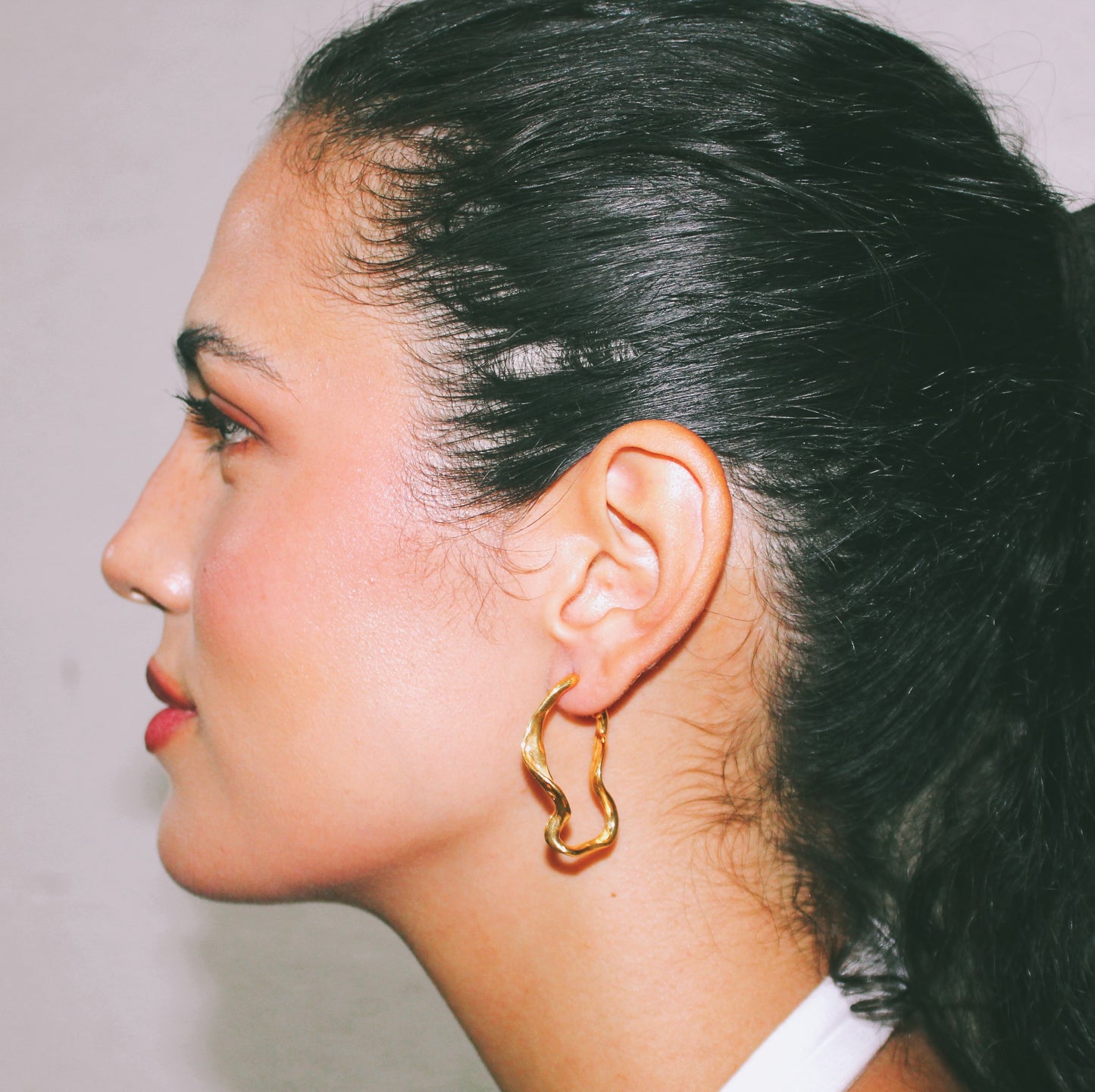 Close-up of a person wearing a gold hoop earring with a neutral background handmade jewelry lisbon