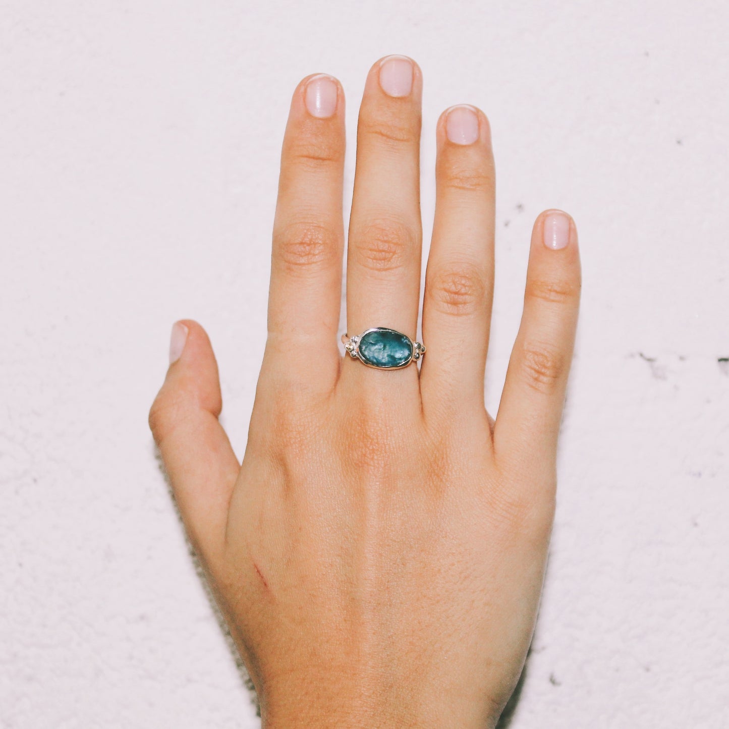 Hand wearing a ring with a blue gemstone on a light background