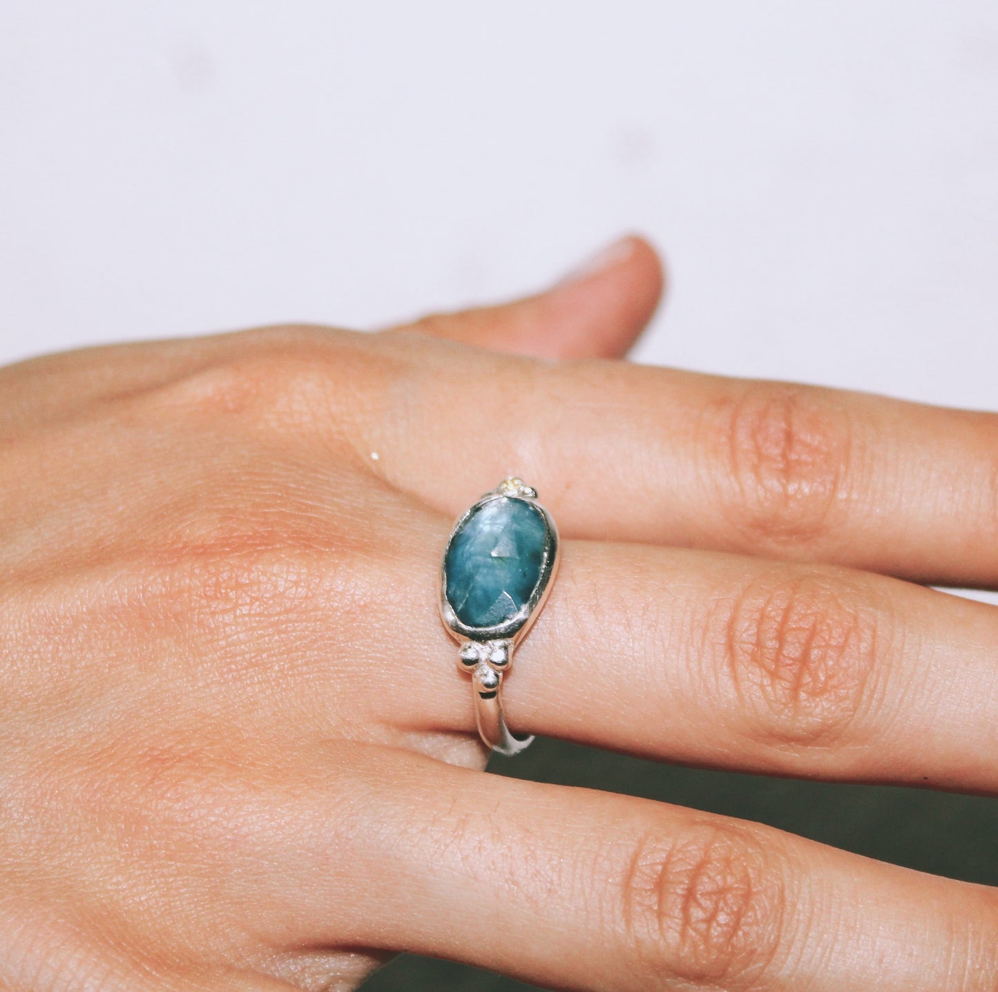 Silver ring with a blue gemstone on a hand against a neutral background