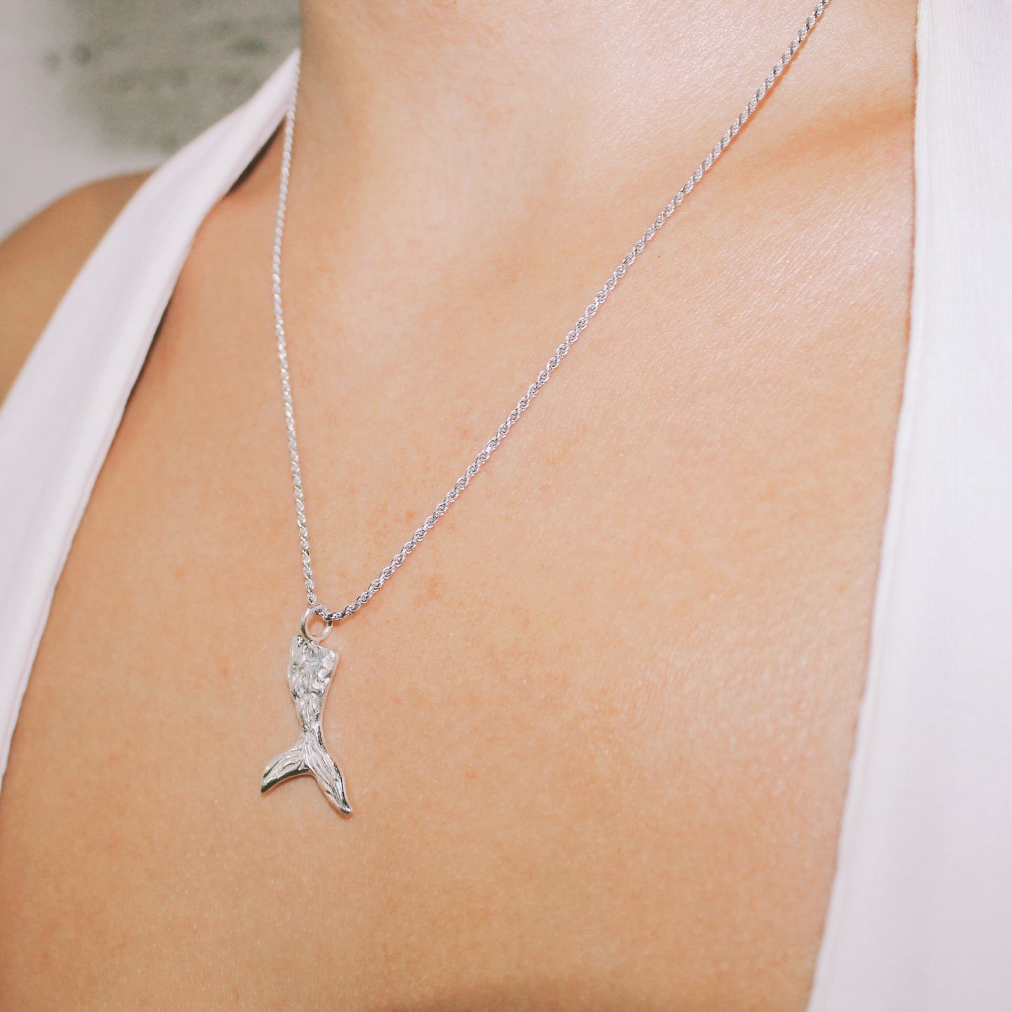 Silver necklace with a mermaid tail pendant on a person wearing a white top. handmade jewelry lisbon