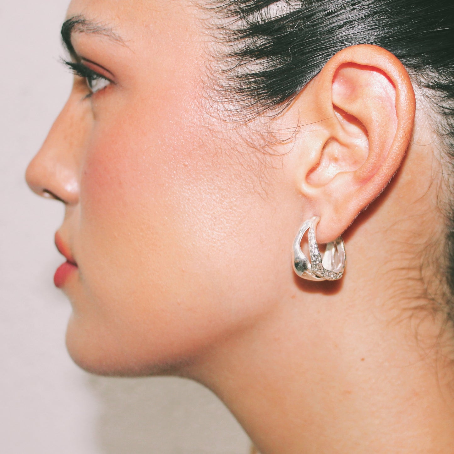 Close-up of a person wearing a silver hoop earring on a plain background