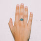 Hand wearing a ring with a blue gemstone on a light background