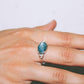 Silver ring with a blue gemstone on a hand against a neutral background