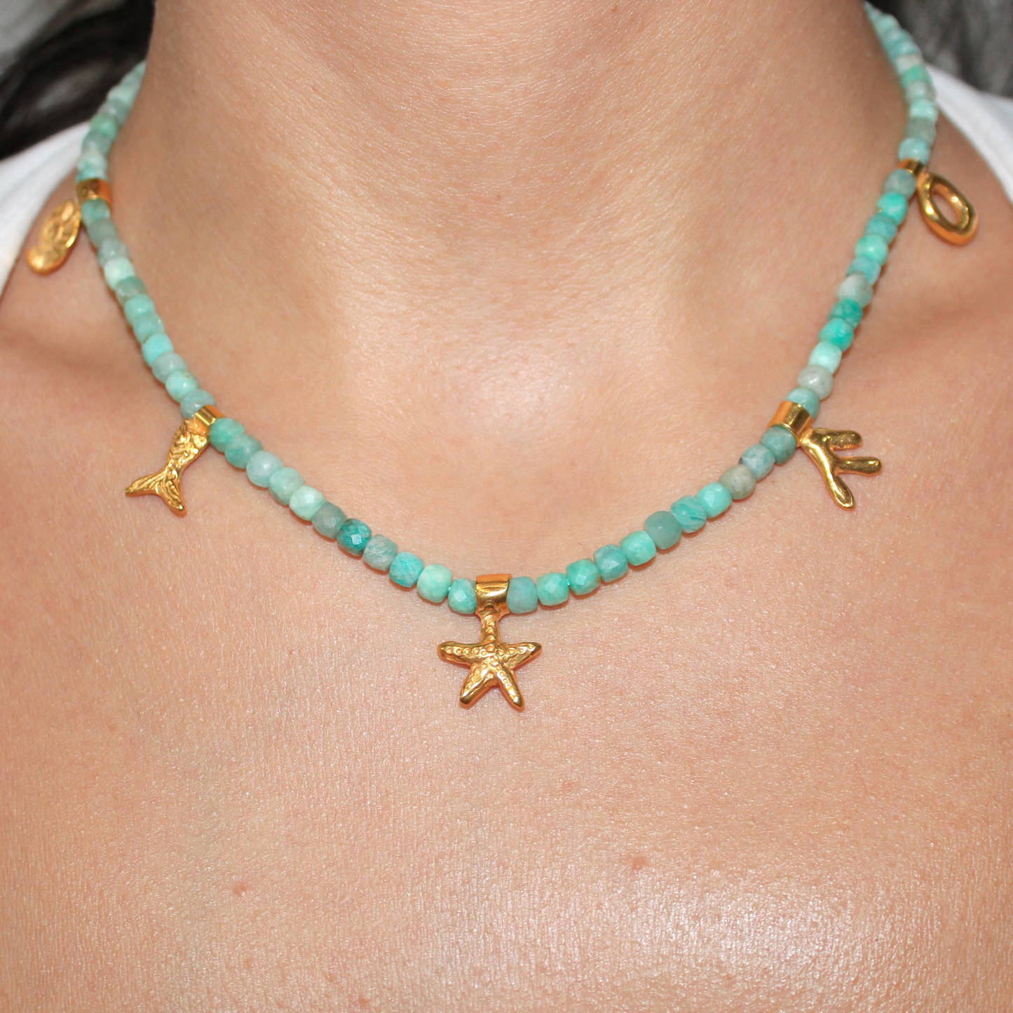 Necklace with aquamarine turquoise beads and gold starfish marine pendants charms on a person's neck.