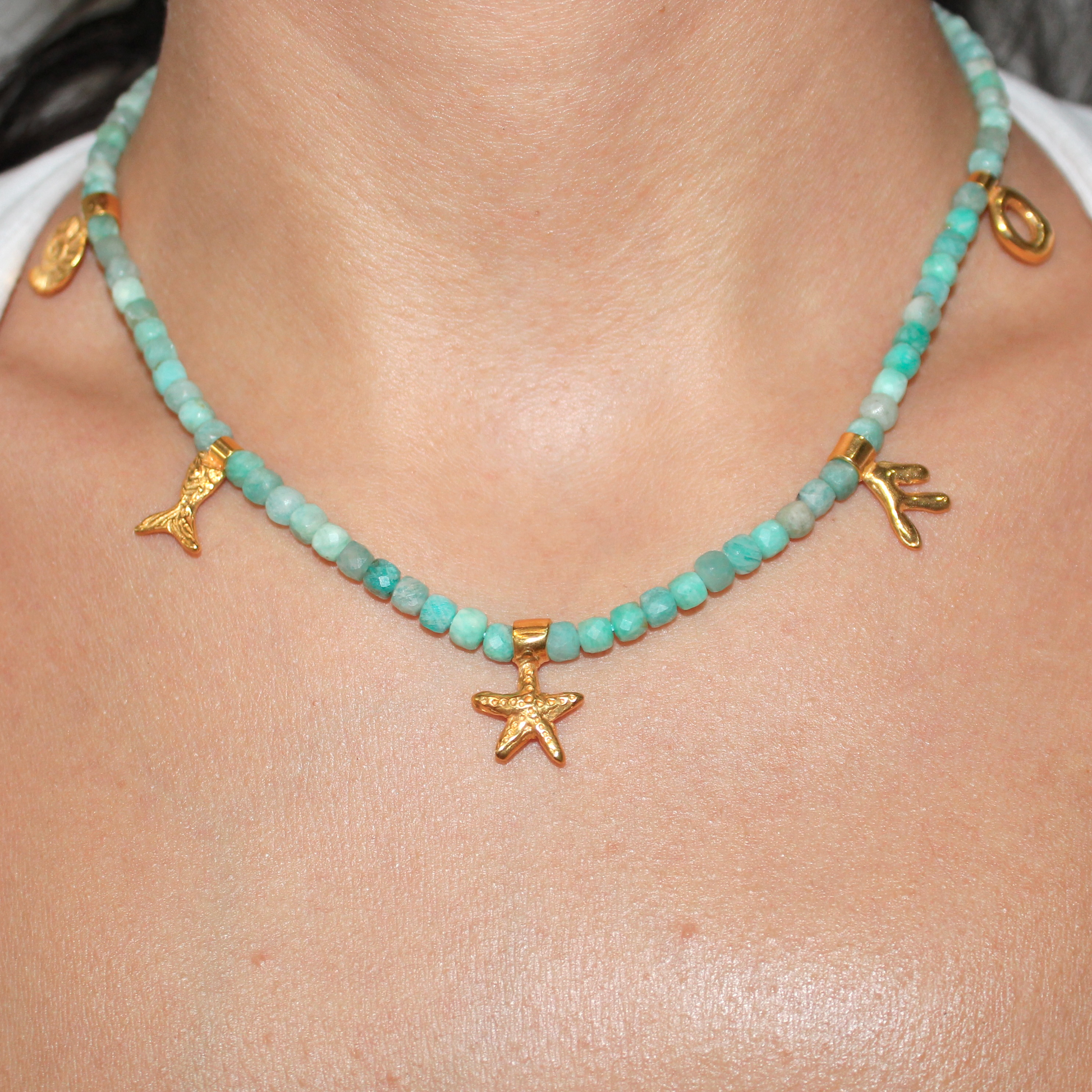 Necklace with aquamarine turquoise beads and gold starfish marine pendants charms on a person's neck.