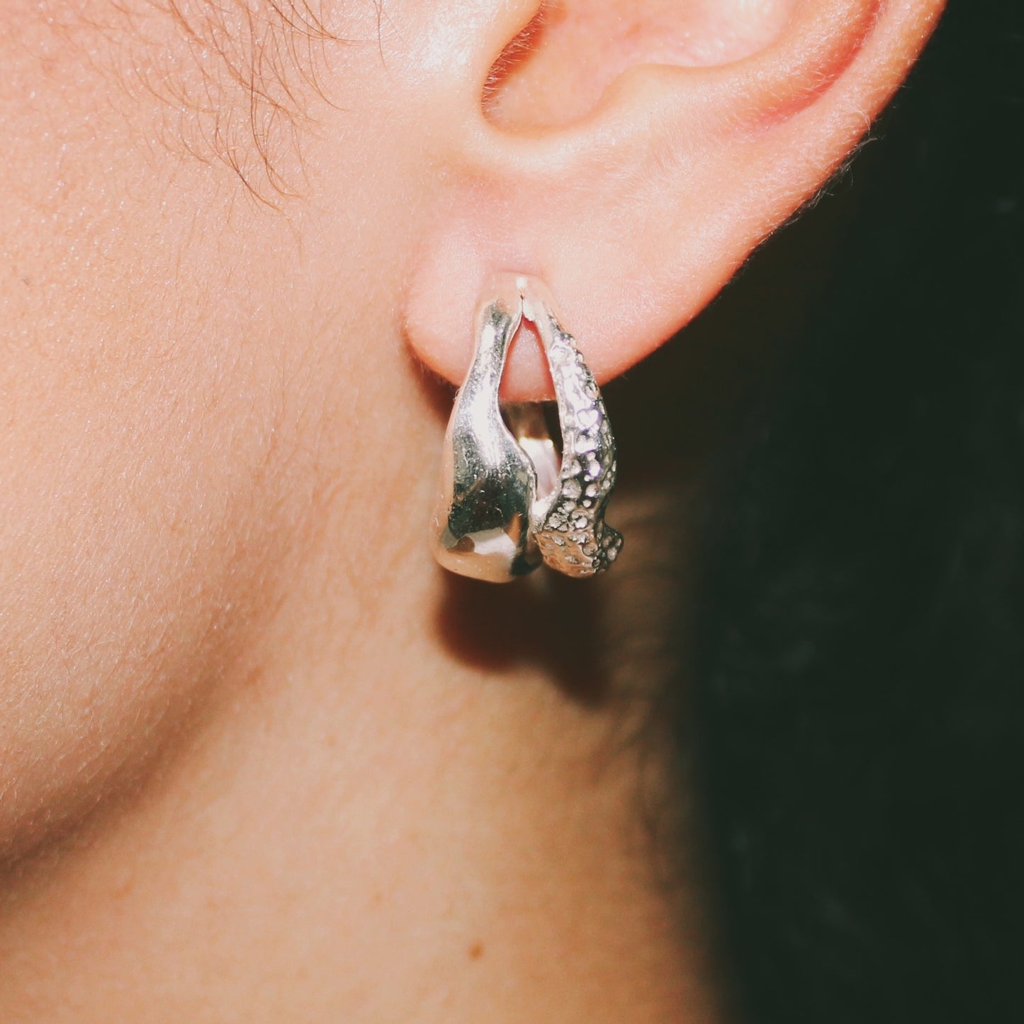 Close-up of a silver earring worn on an ear with a dark background